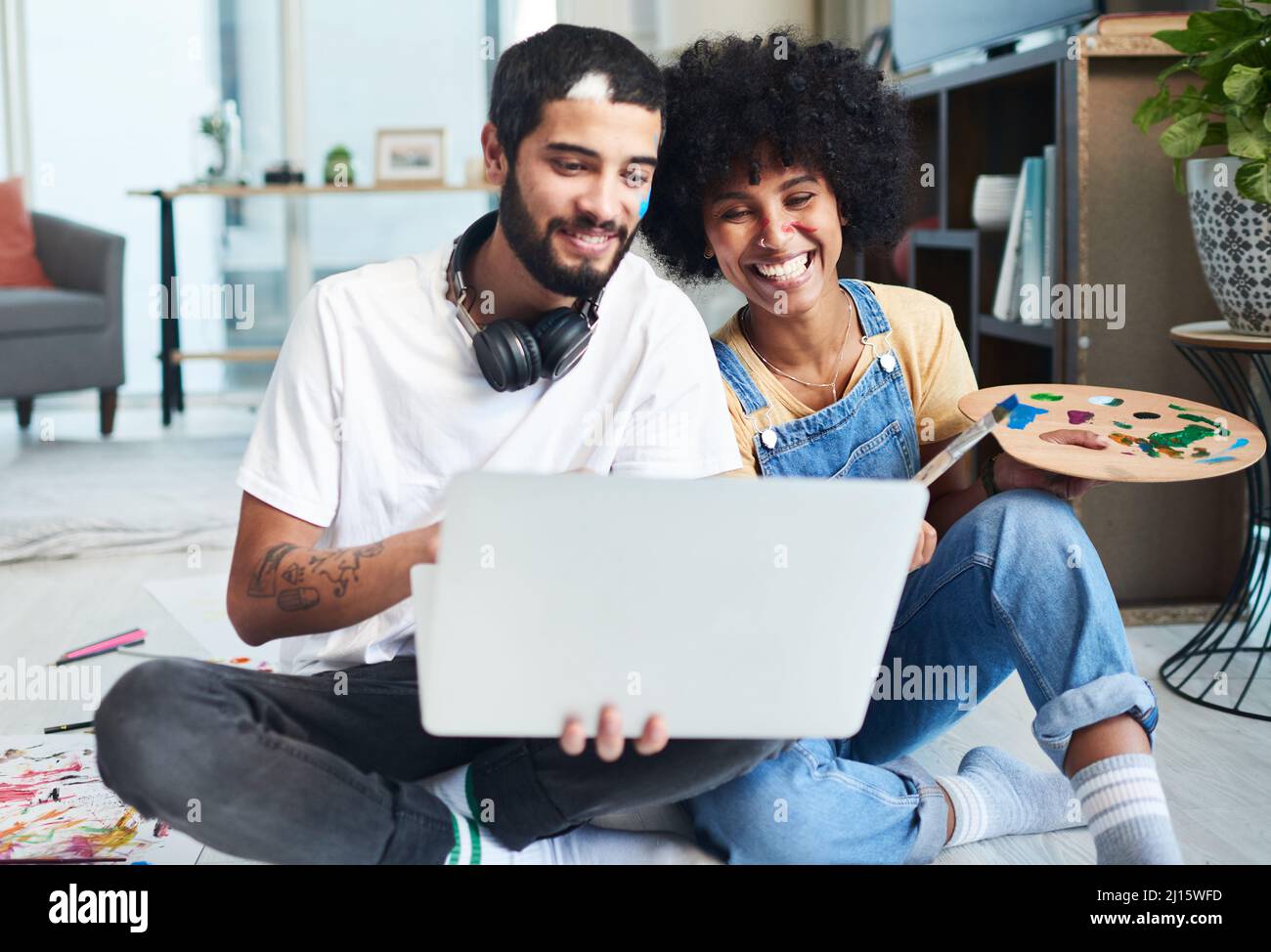 Das Internet ist voll von lustigen Aktivitäten für Paare. Aufnahme eines jungen Paares, das einen Laptop benutzt, während es zu Hause malt. Stockfoto