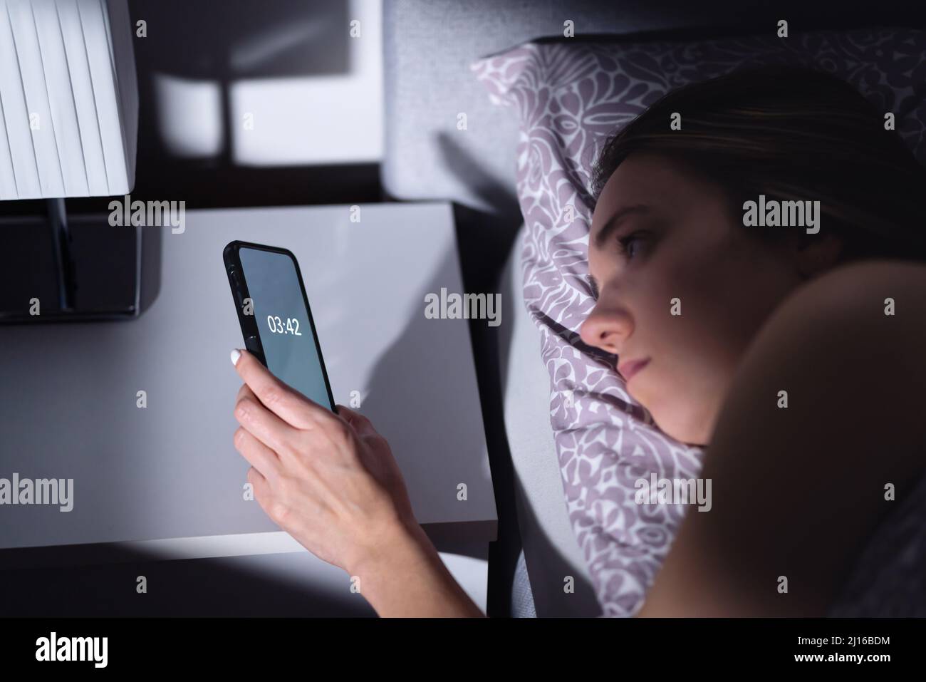 Schlaflosigkeit. Schlaflose Frau, die die Zeit nicht in der Nacht schlafen. Traurige müde Person mit Störung im Bett. Telefonuhr. Ein schlechter Traum. Stockfoto