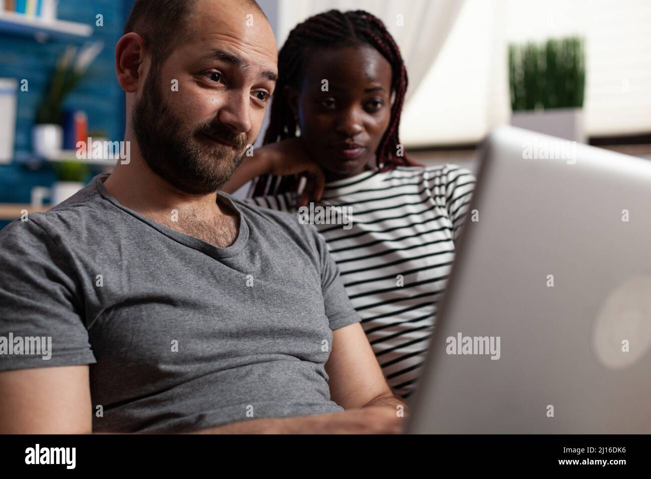 Junge Erwachsene interracial paar Blick auf Computer-Bildschirm, während die Überprüfung Social-Network-Feed. Menschen surfen auf einem modernen Laptop, während sie zusammen auf dem Sofa im Wohnzimmer zu Hause sitzen Stockfoto