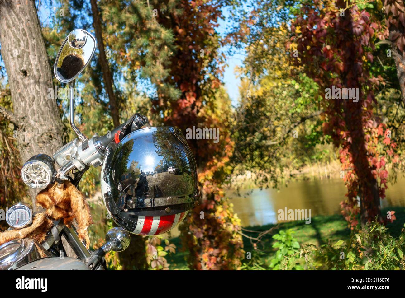 Helm, der am Lenkrad auf dem Hintergrund des Herbstwaldes und des Flusses hängt. Spiegelvisier Stockfoto