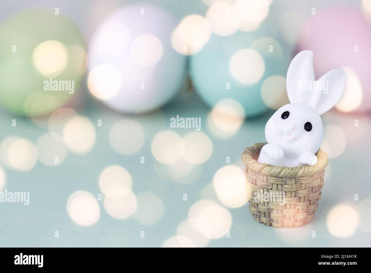 Osterhintergrund. Osterhase in einem Korb vor dem Hintergrund von farbigen Eiern. Postkarte in Pastellfarben mit Bokeh. Speicherplatz kopieren Stockfoto