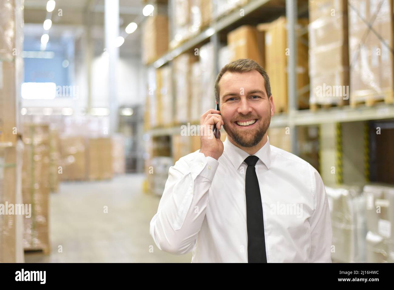 Portrait freundlicher Geschäftsmann/Manager in Anzug am Telefon im Lager eines Unternehmens Stockfoto