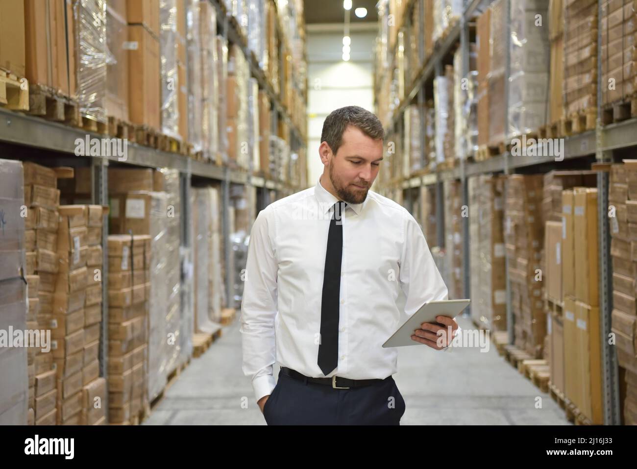 Portrait freundlicher Geschäftsmann/Manager im Anzug, der im Lager eines Unternehmens arbeitet - Kontrolle der Lagerbestände Stockfoto