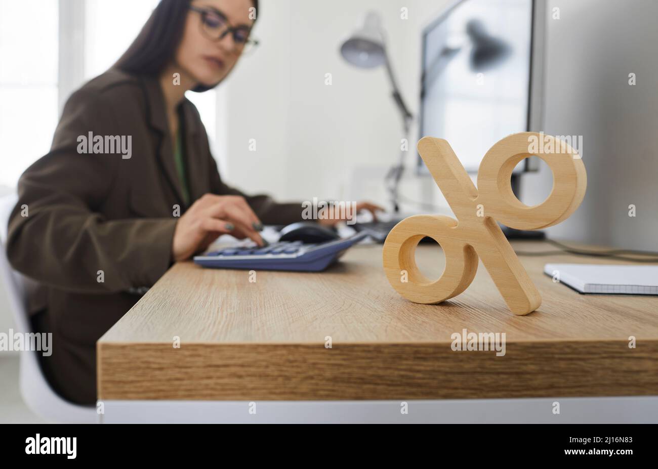 Nahaufnahme des hölzernen Prozentzeichens, das auf dem Tisch auf dem Hintergrund der Frau steht, die auf dem Rechner zählt. Stockfoto