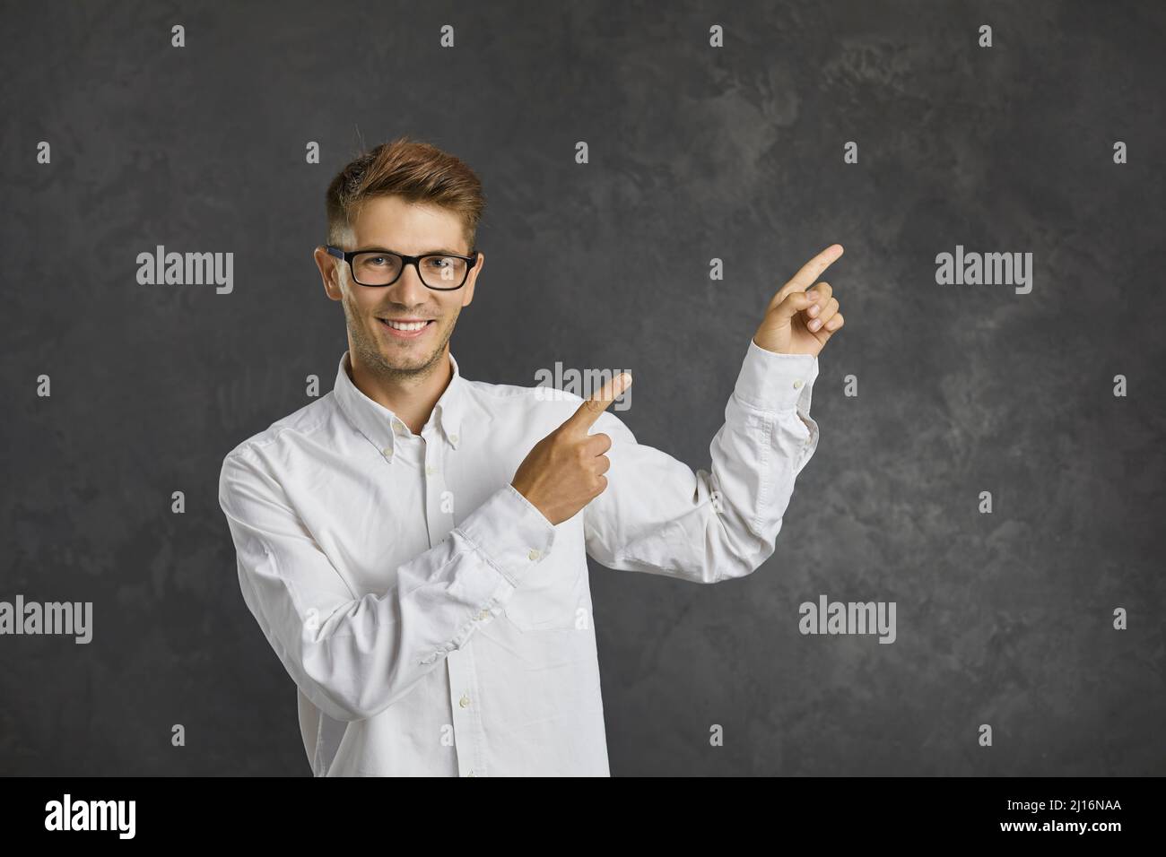 Freundlicher Mann mit lächelndem Ausdruck zeigt seine Zeigefinger auf die Seite auf grauem Hintergrund. Stockfoto