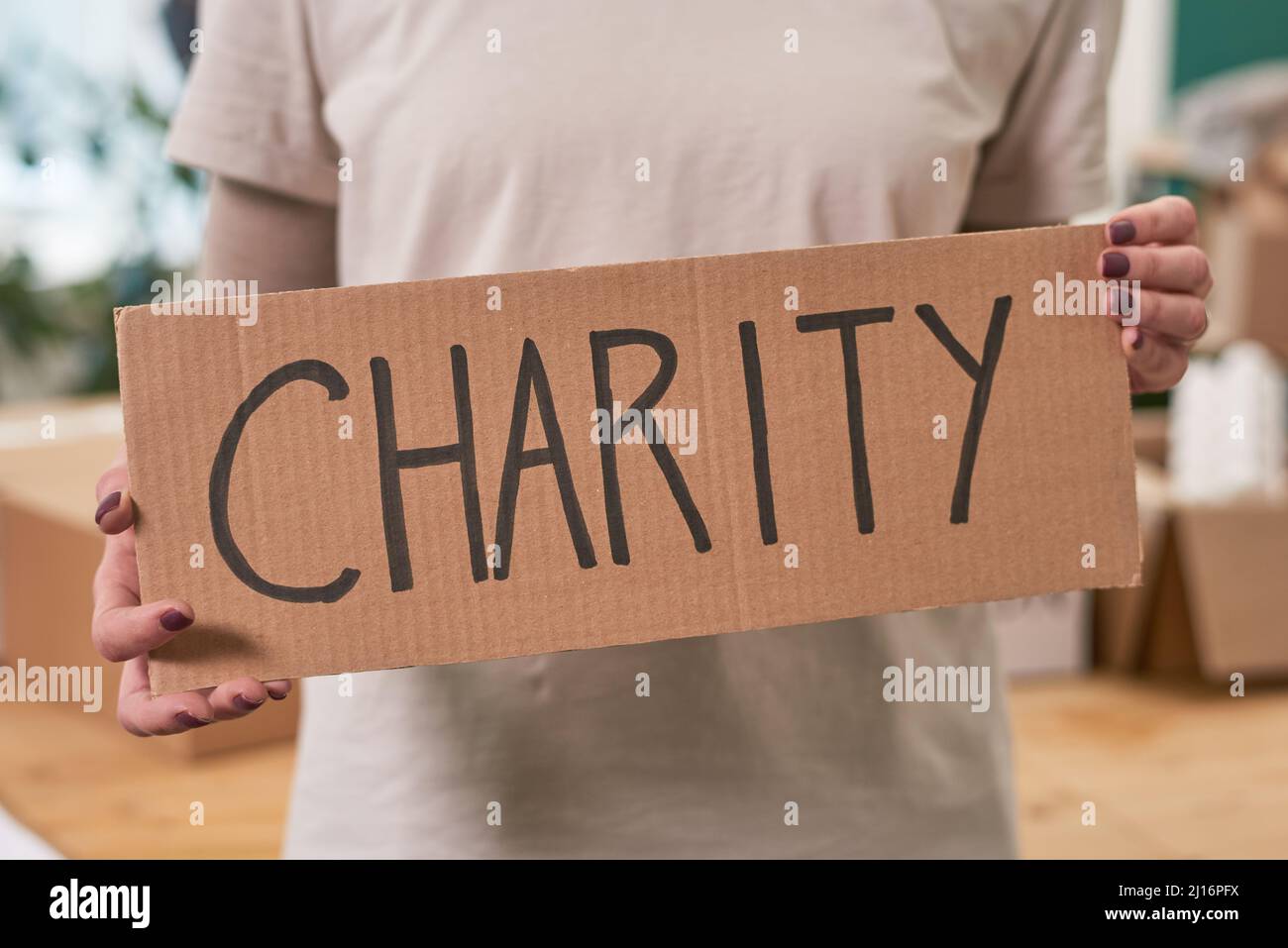 Mittellange Aufnahme einer nicht erkennbaren Frau in einem beigefarbenen T-Shirt mit einem Schild aus Pappe und einem Wort der Wohltätigkeitsorganisation Stockfoto