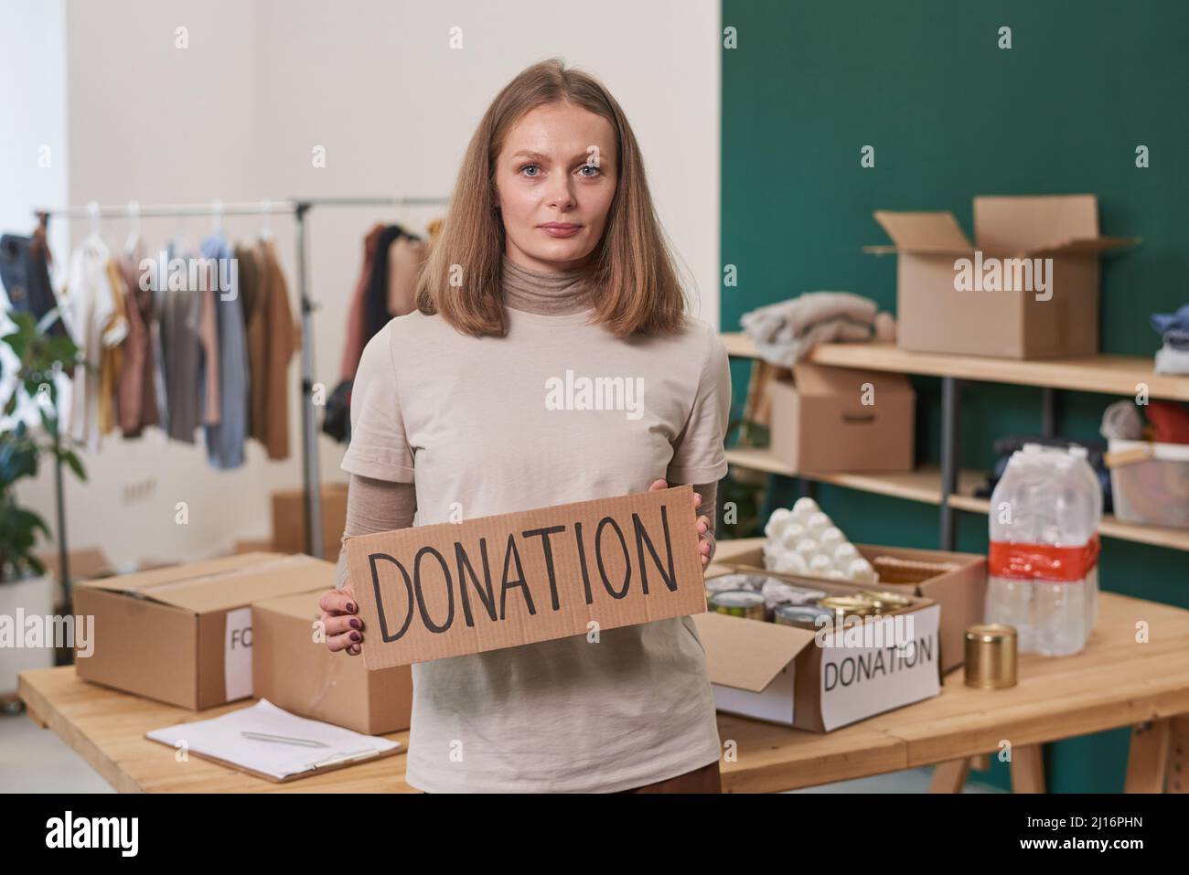 Mittleres Porträt einer modernen reifen Frau, die ein beiges T-Shirt mit einem Schild aus Pappe trägt, mit einem Wort, das auf die Kamera schaut Stockfoto