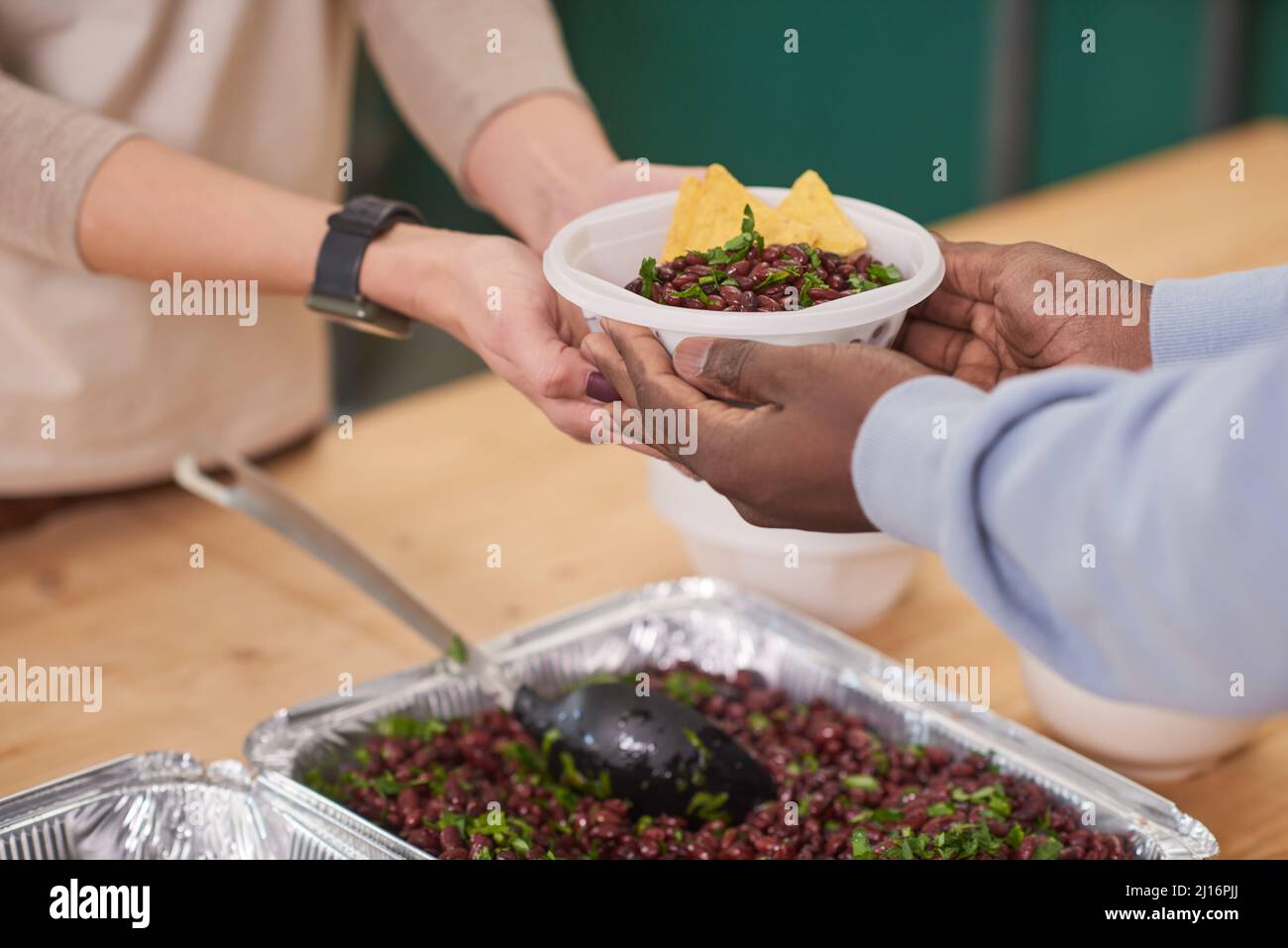 Mittlere Nahaufnahme eines nicht erkennbaren Freiwilligen, der den Begünstigten in der Kantine der Wohltätigkeitsorganisation Teller mit Essen übergab Stockfoto