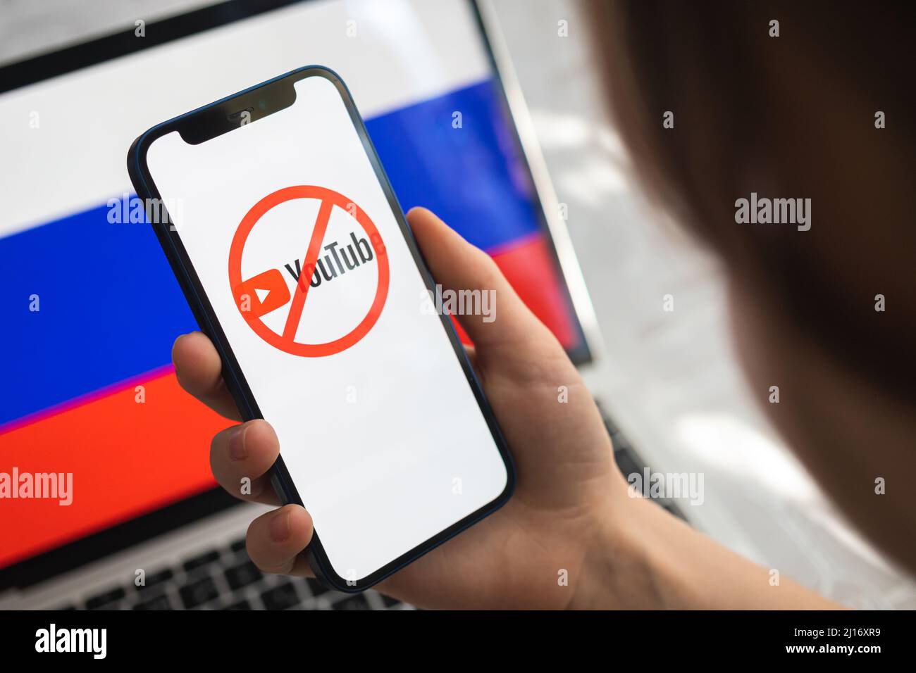 Poltava, Ukraine - 23. März 2022: Frau versucht, Youtube in Russland zu nutzen. Smartphone mit verbotenem Logo von Youtube und Hintergrund der russischen Flagge Stockfoto