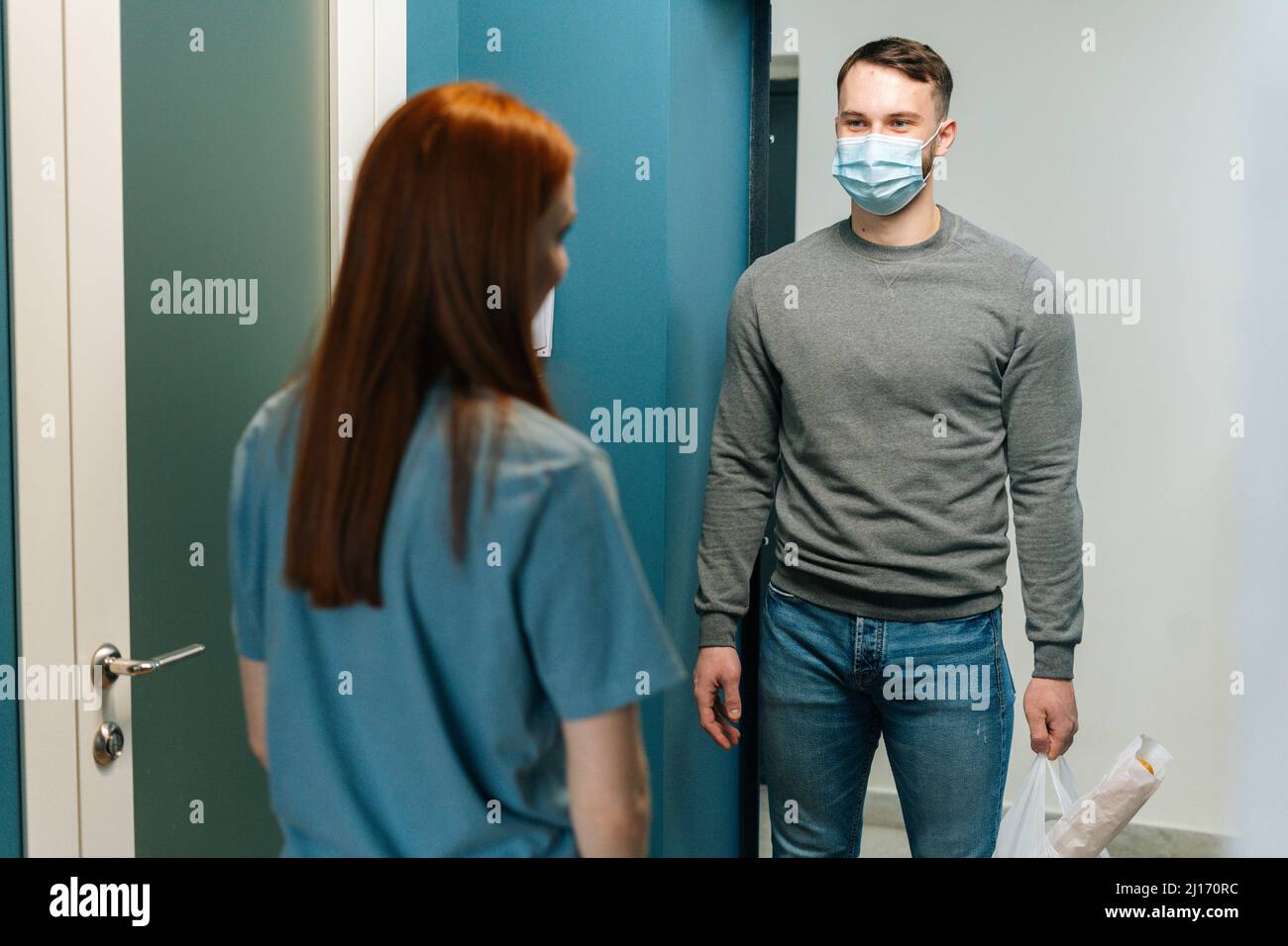 Courier männlich trägt schützende Gesichtsmaske liefert Lebensmittelbeutel an weibliche Hausfrau Kunde auf Tür zu Hause. Stockfoto