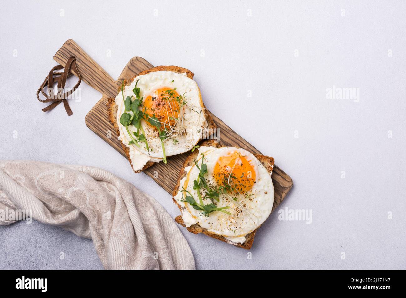 Blick von oben auf Sandwich mit Spiegeleiern, Toast, Luzerne und grünen Erbsensprossen mikrogrün zum Frühstück auf grauem Beton Hintergrund Stockfoto