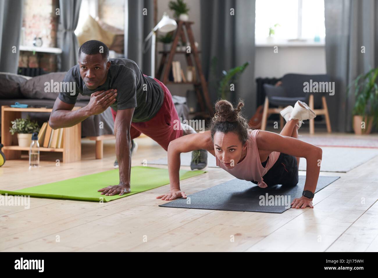 Sportlicher junger schwarzer Mann und kaukasische Frau, die Kräftigungsübungen im Wohnzimmer zu Hause machen Stockfoto