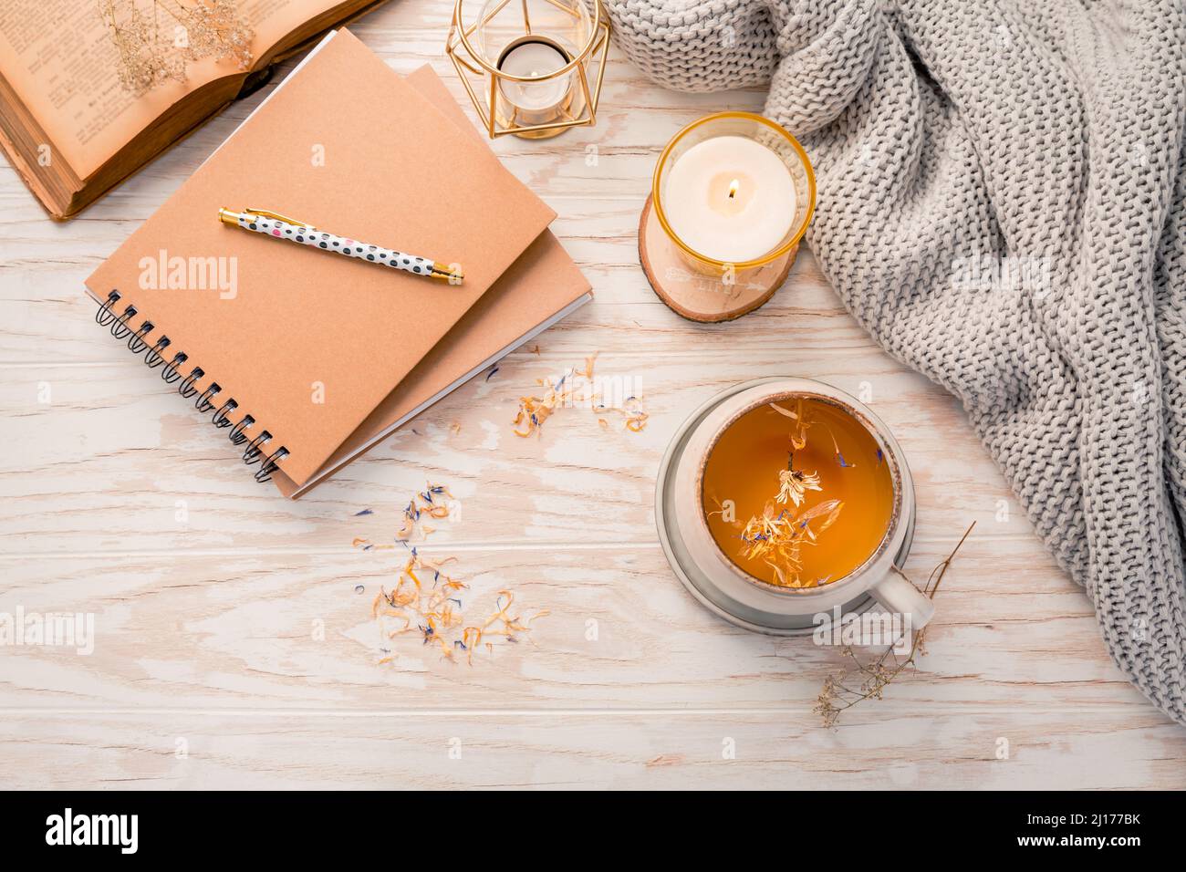 Heißer Kräutertee mit Notizblock, Kerze, Buch und Decke. Gemütlicher und hygge Lebensstil Stockfoto
