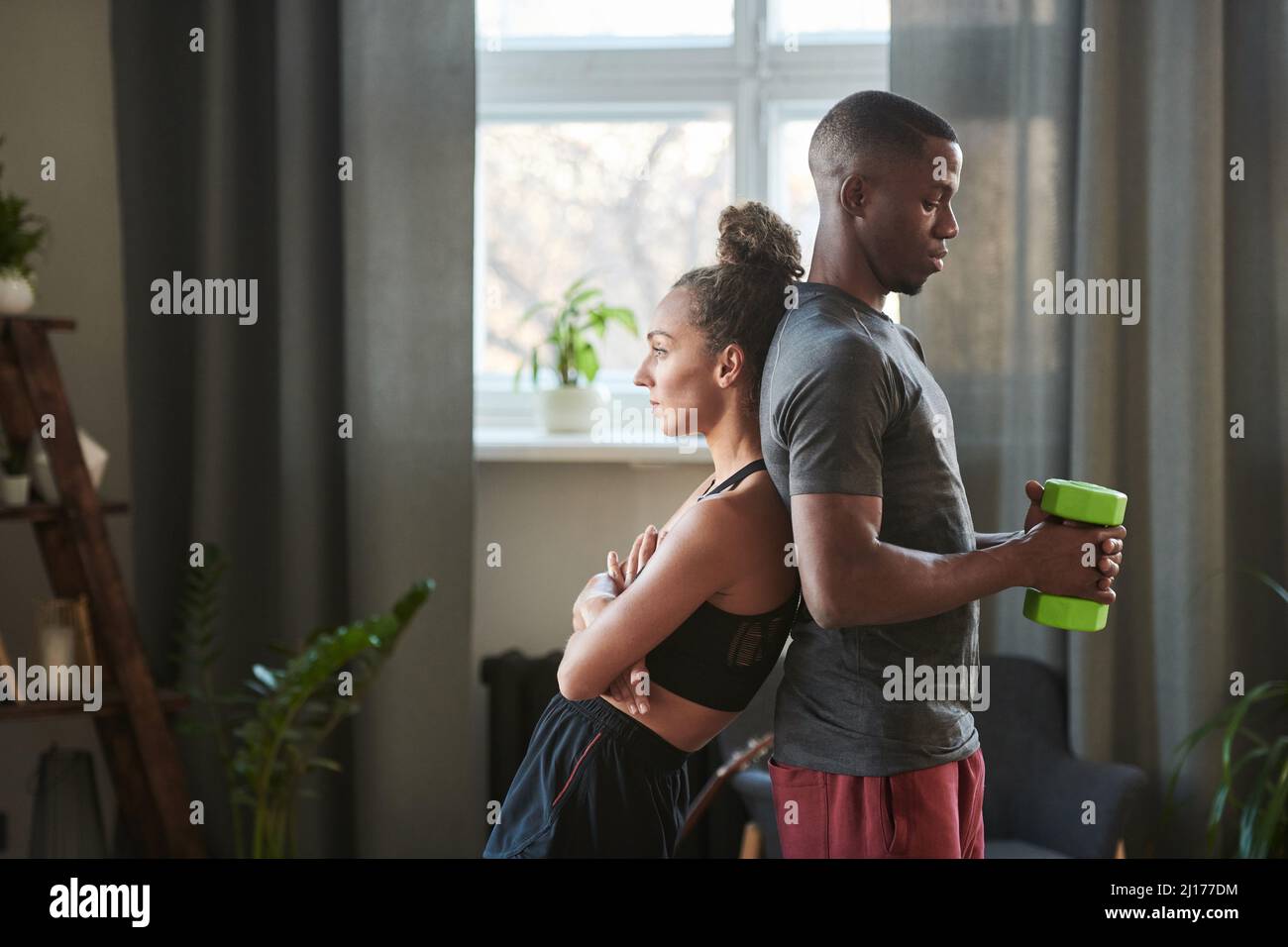 Moderner sportlicher schwarzer Mann und kaukasische Frau in der Liebe, die sich zu Hause im Loft-Wohnzimmer zurücklehnen Stockfoto