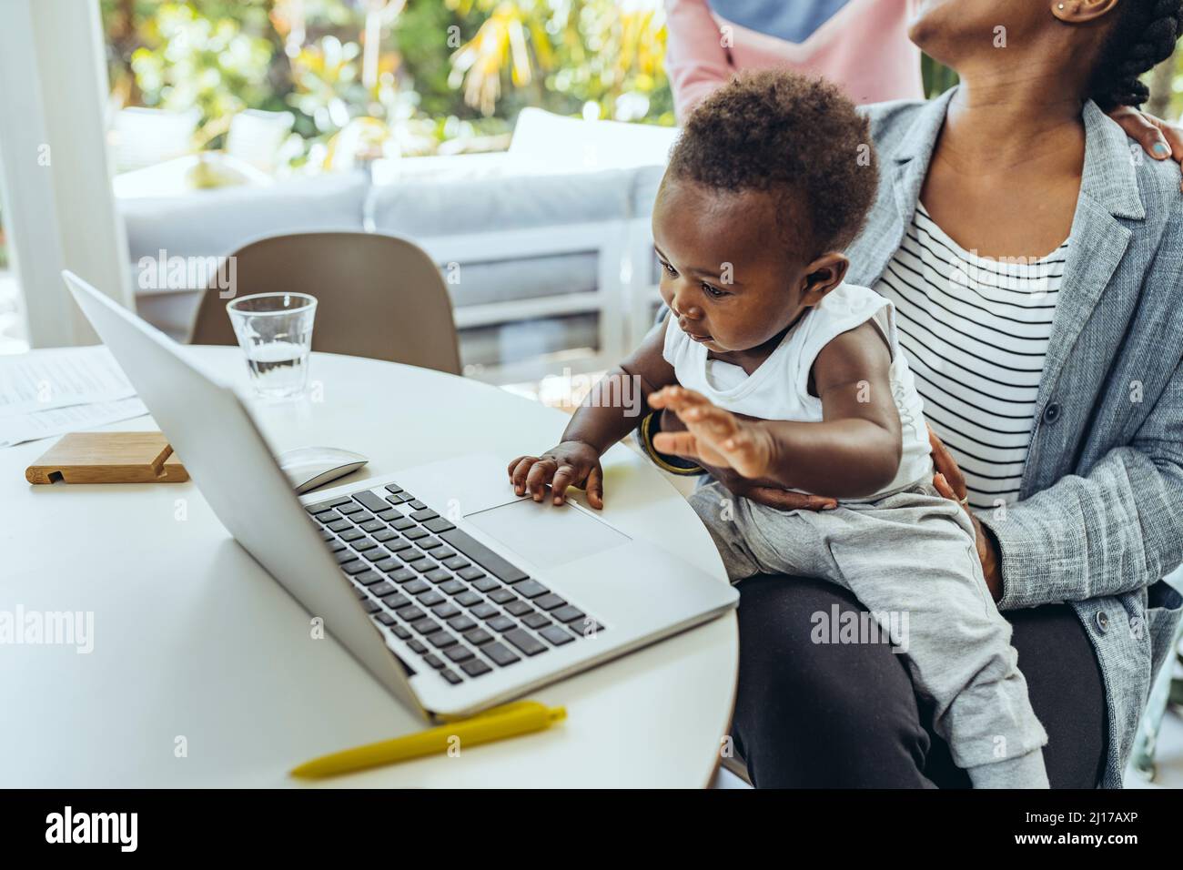 Mutter mit Baby auf dem Schoß mit Laptop im Esszimmer Stockfoto