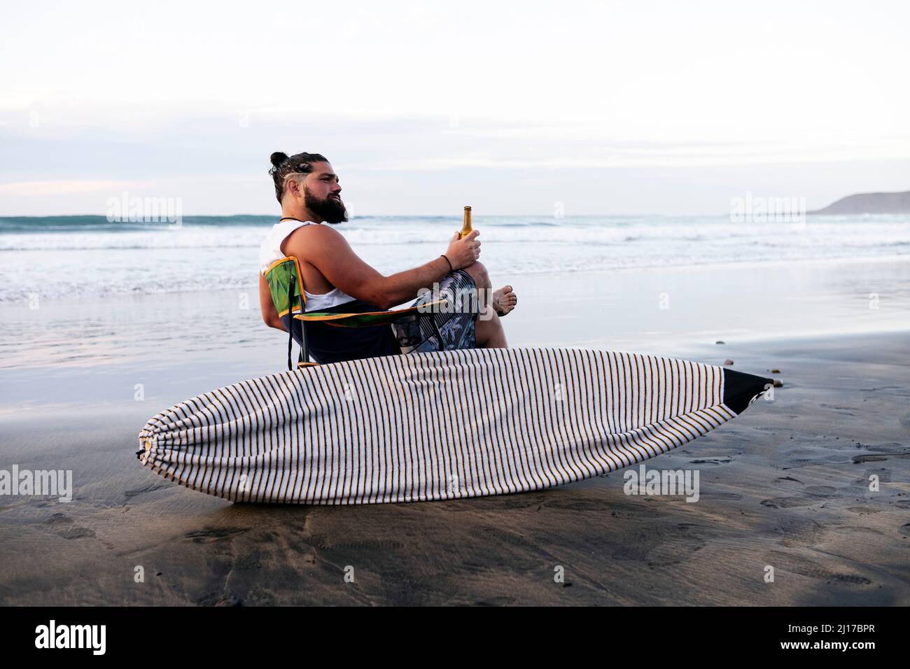 Mann, der am überdachten Surfbrett am Strand sitzt Stockfoto