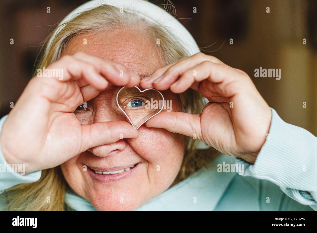 Lächelnde ältere Frau, die durch einen herzförmigen Ausstecher schaut Stockfoto