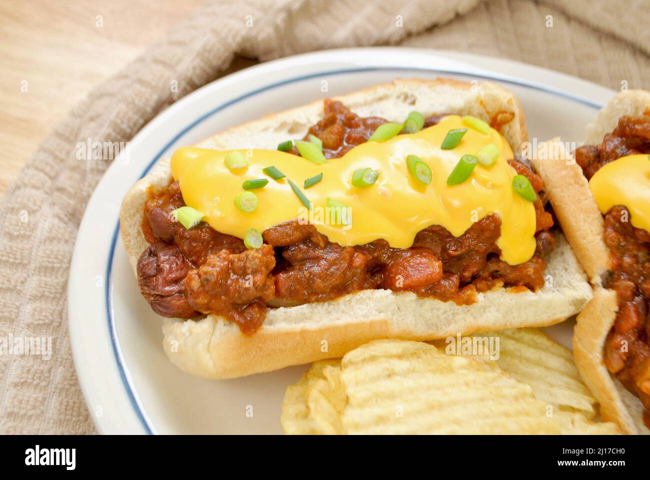 Beladen Chilli Dog mit Cheddar-Käse und Scallion serviert mit gewellten Kartoffelchips Stockfoto