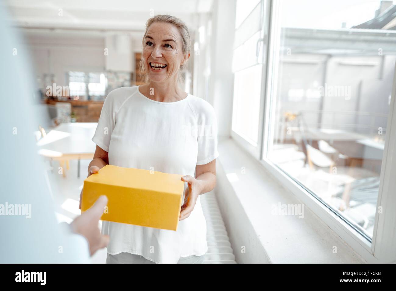 Fröhliche Geschäftsfrau erhält Schachtel vom Geschäftsmann im Büro Stockfoto