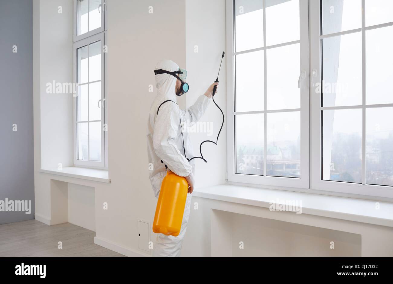 Männliche Desinfektionsmittel im Schutzanzug desinfiziert durch Sprühen kontaminierter Bereiche des Hauses. Stockfoto