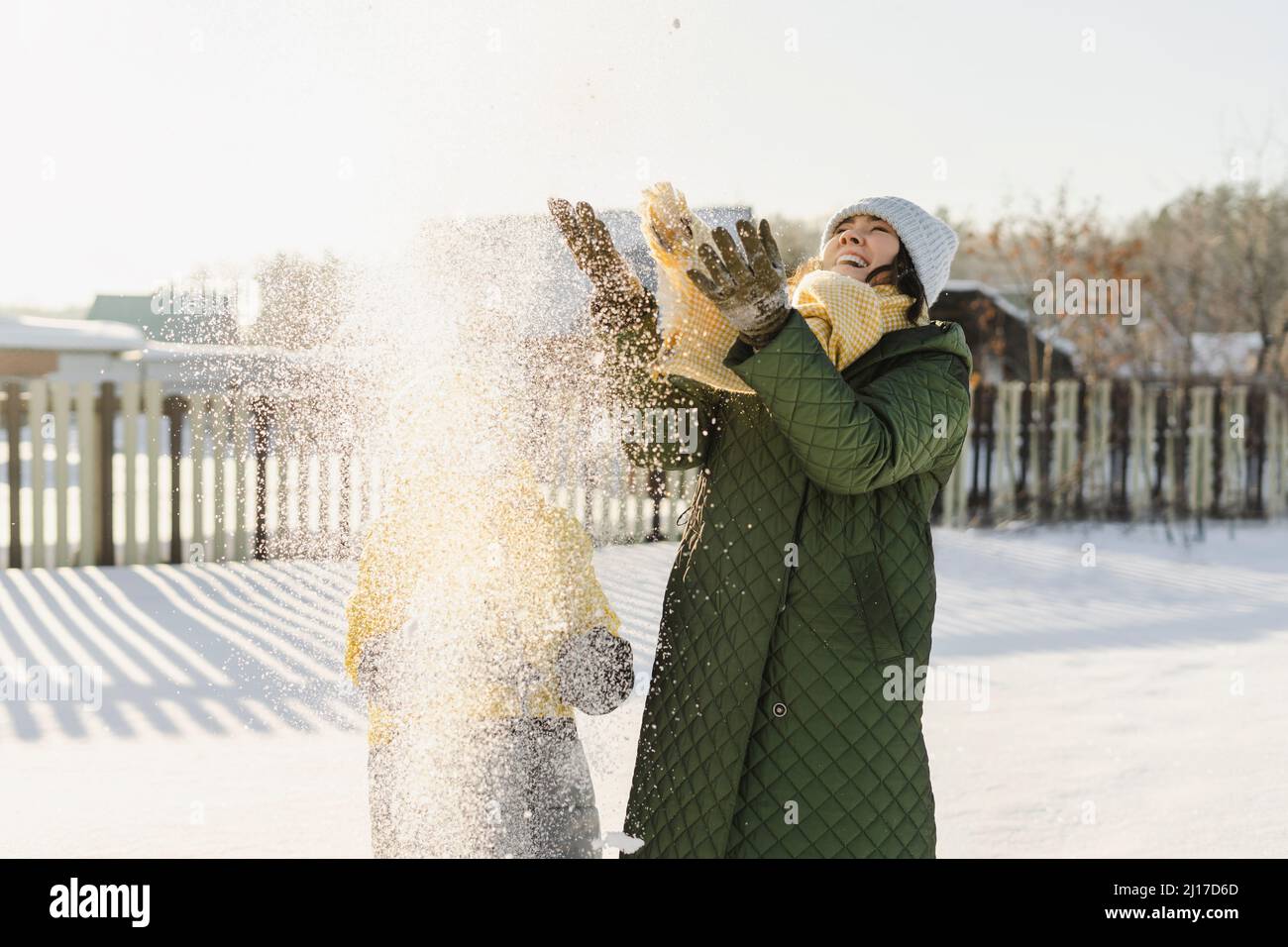 Fröhliche Mutter mit Sohn, der im Winter Schnee wirft Stockfoto