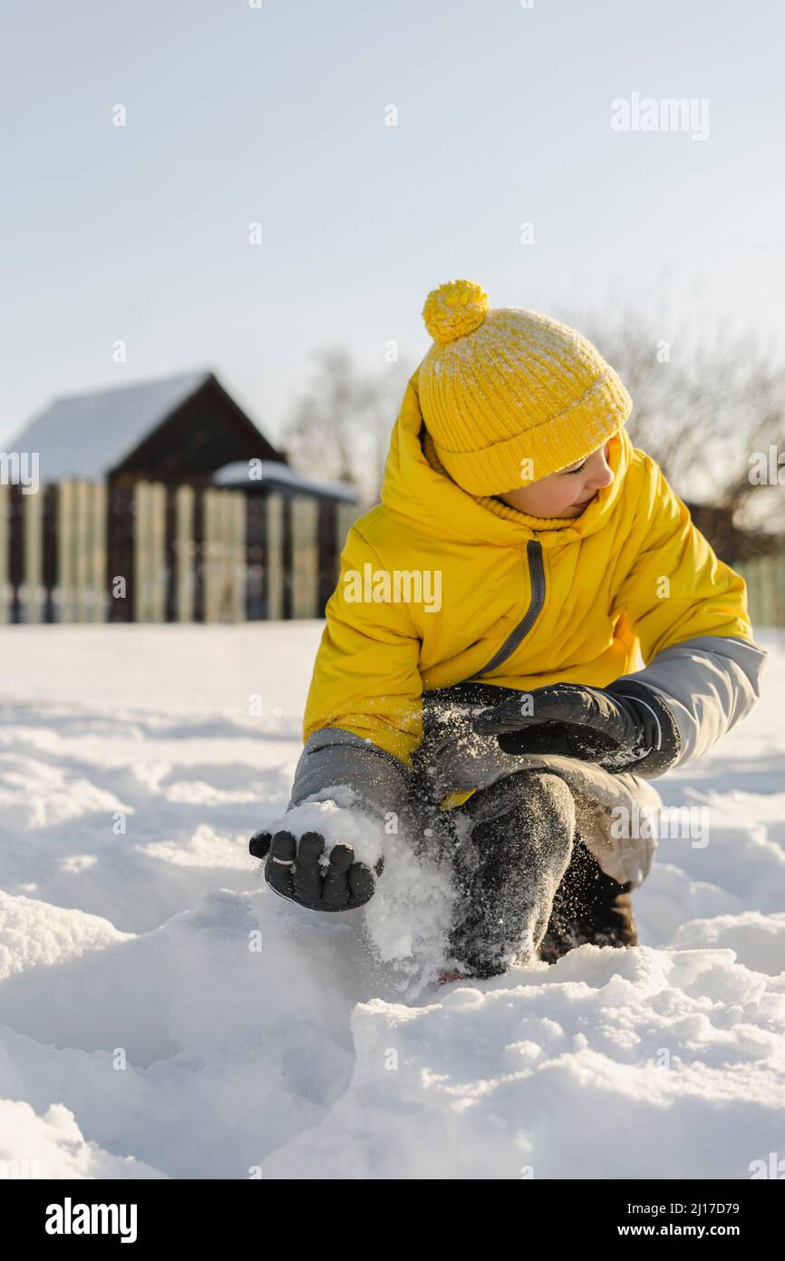 Fröhlicher Junge mit Strickmütze, der im Winter mit Schnee spielt Stockfoto
