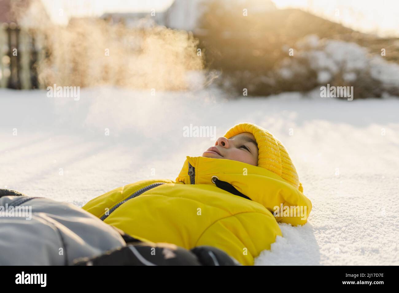 Junge mit Strickmütze, die im Winter auf Schnee liegt Stockfoto