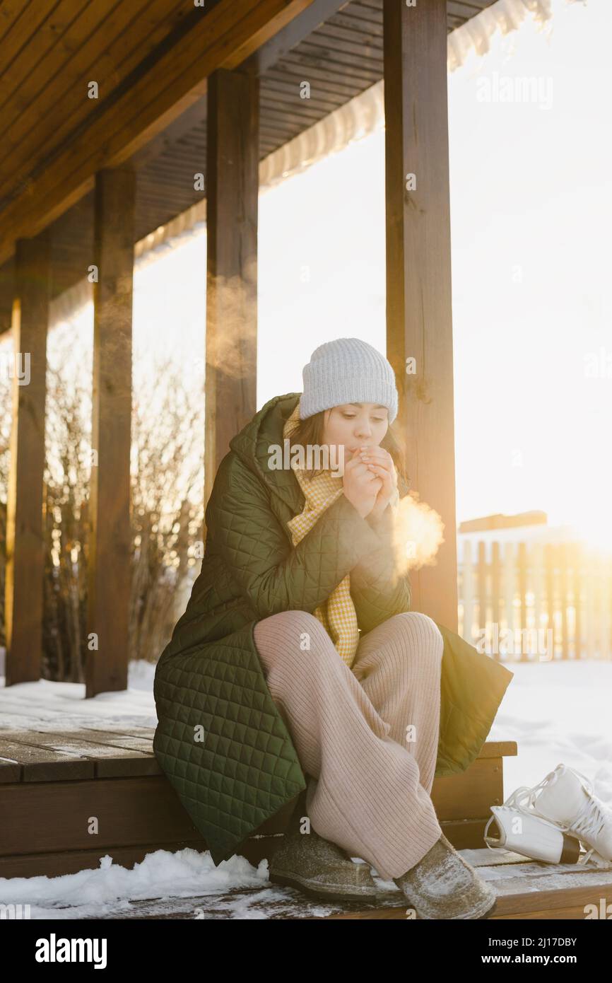 Frau, die auf der Veranda des Hauses im verschneiten Garten sitzt Stockfoto