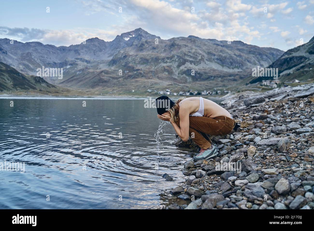 Frau, die am Seeufer, Splugen Pass, Sondrio, Italien, das Gesicht wascht Stockfoto
