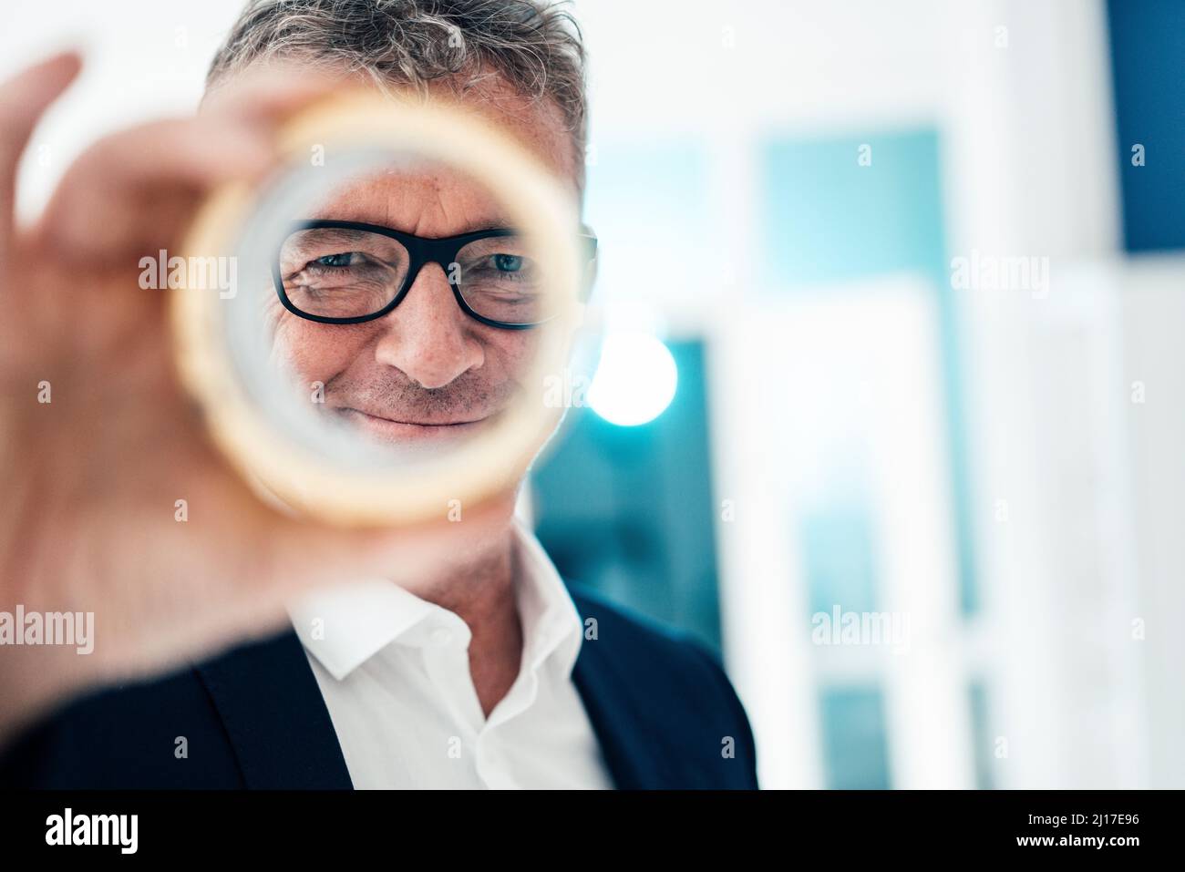 Lächelnder Geschäftsmann mit Brillen, die durch ein kreisförmiges Objekt schauen Stockfoto