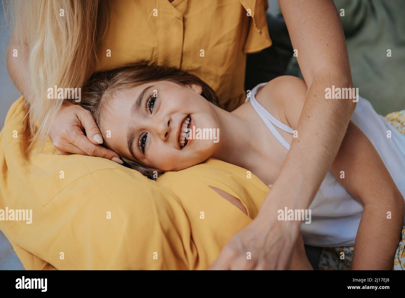 Lächelnde Tochter, die auf dem Schoß der Mutter auf der Terrasse liegt Stockfoto