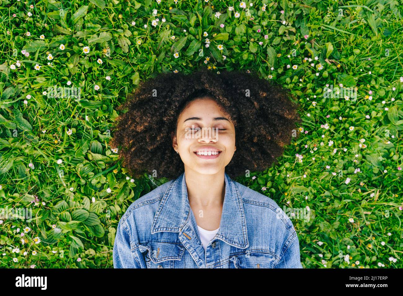 Lächelnde Afro-Frau, die auf grün blühenden Pflanzen auf der Wiese liegt Stockfoto