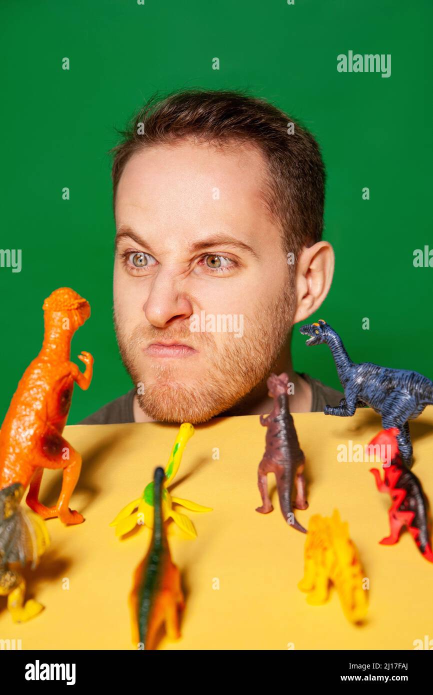 Junger Mann, der vor Dinosaurierfiguren ein wütendes Gesicht macht Stockfoto