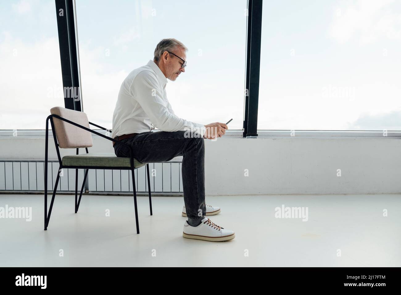 Geschäftsmann mit Smartphone auf dem Stuhl im Startup-Büro sitzen Stockfoto