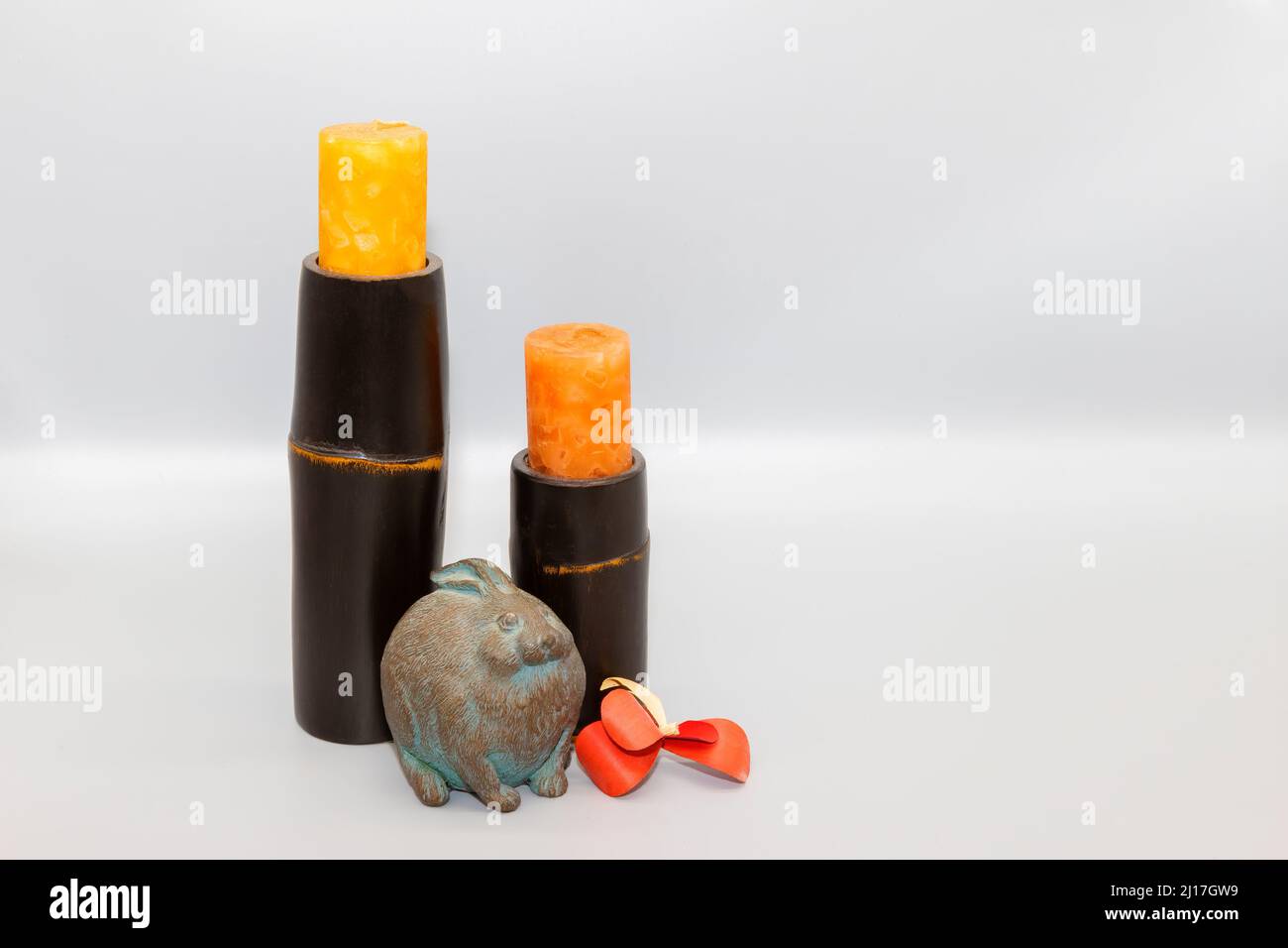 Viel Platz zum Kopieren in diesem Stillleben mit Wohnkultur aus Kerzen, Steinkaninchen und einer Holzblume. Stockfoto