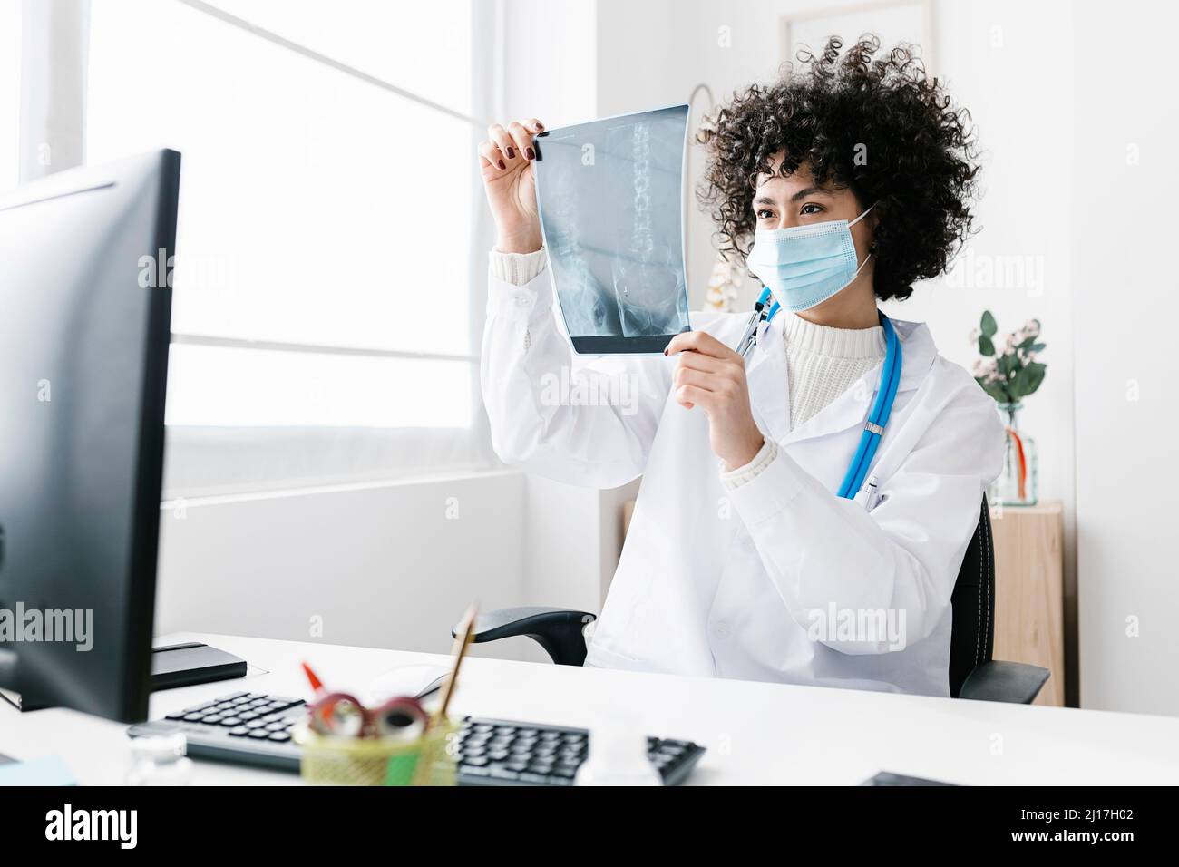 Arzt trägt eine schützende Gesichtsmaske und analysiert den Röntgenbericht in der Klinik Stockfoto