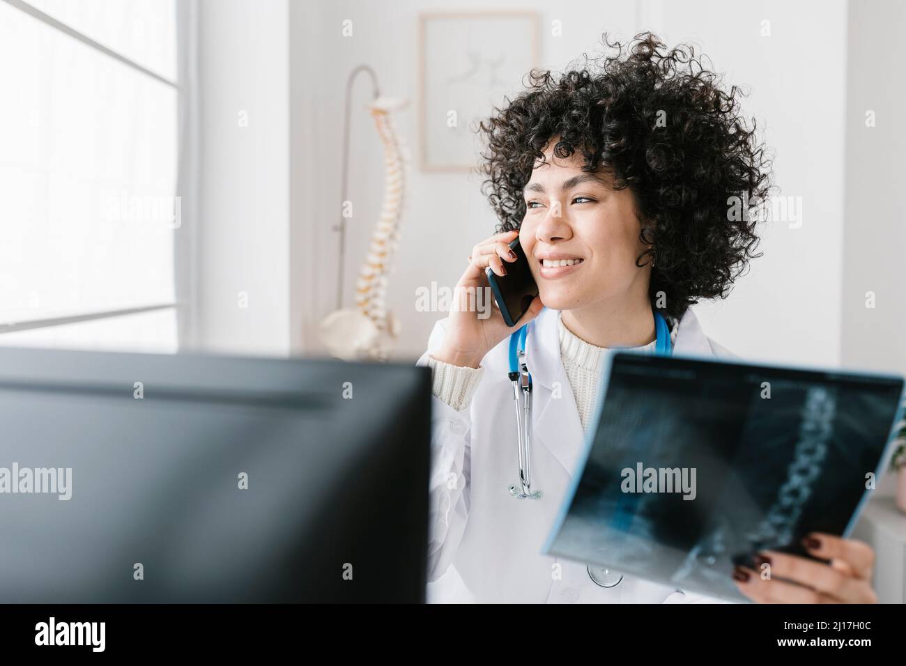 Lächelnder Arzt mit Röntgenaufnahmen auf dem Smartphone in der medizinischen Klinik Stockfoto
