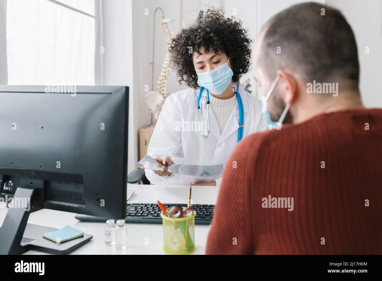 Arzt mit Gesichtsschutzmaske, der dem Patienten in der Klinik den Röntgenbericht erklärt Stockfoto