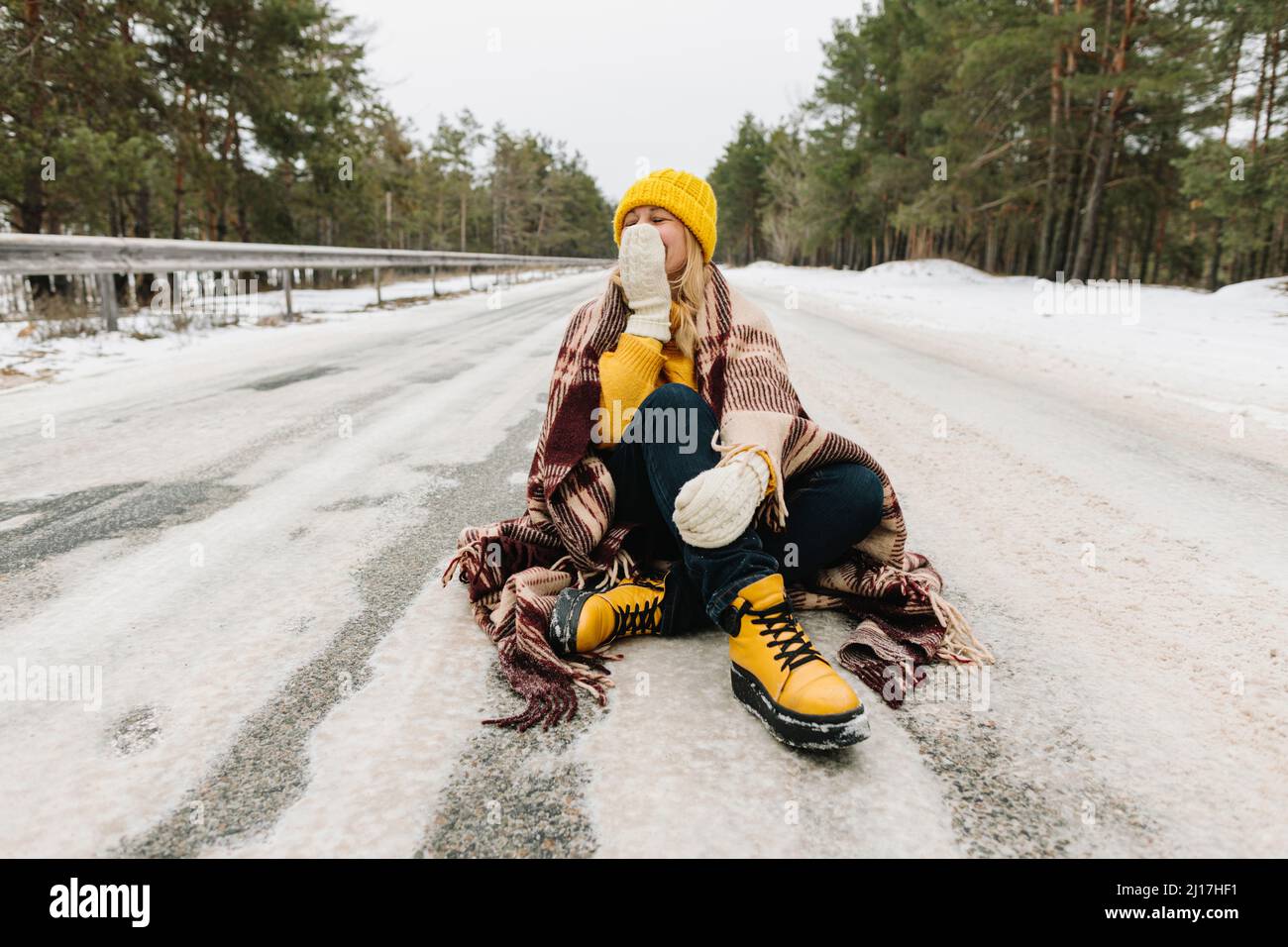 Glückliche Frau mit Decke auf verschneite Straße sitzen Stockfoto