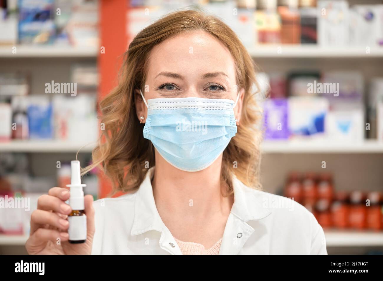 Apothekerin trägt eine schützende Gesichtsmaske mit einer Flasche Nasenspray im Apothekengeschäft Stockfoto