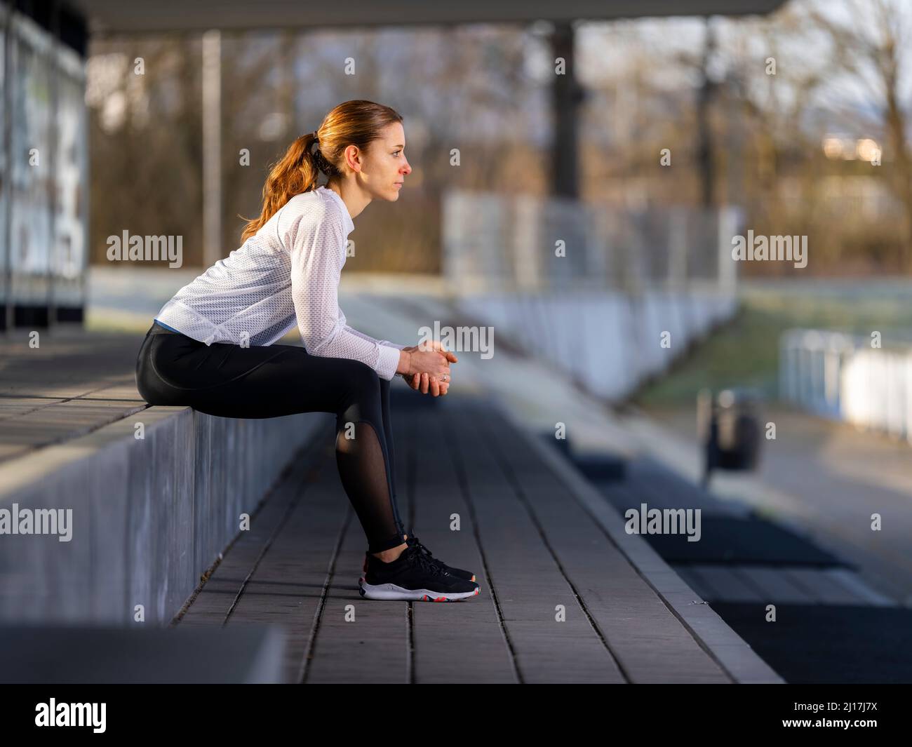 Nachdenkliche Frau, die mit den Händen auf dem Fußpfad zusammengeklemmt sitzt Stockfoto