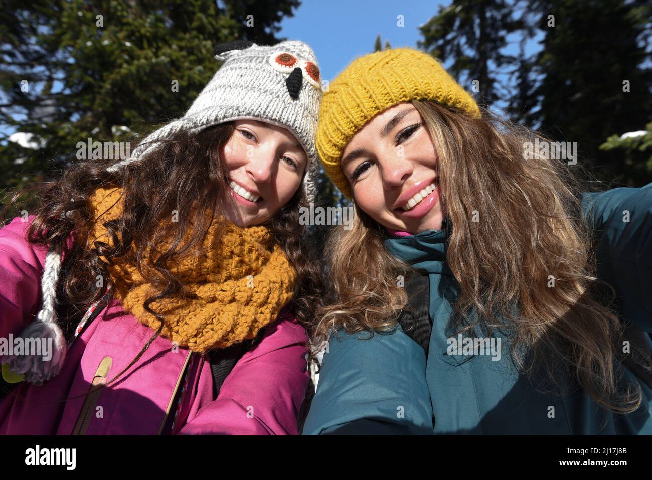 Lächelnde Frauen mit langen Haaren tragen Strickmütze im Winter an sonnigen Tagen Stockfoto