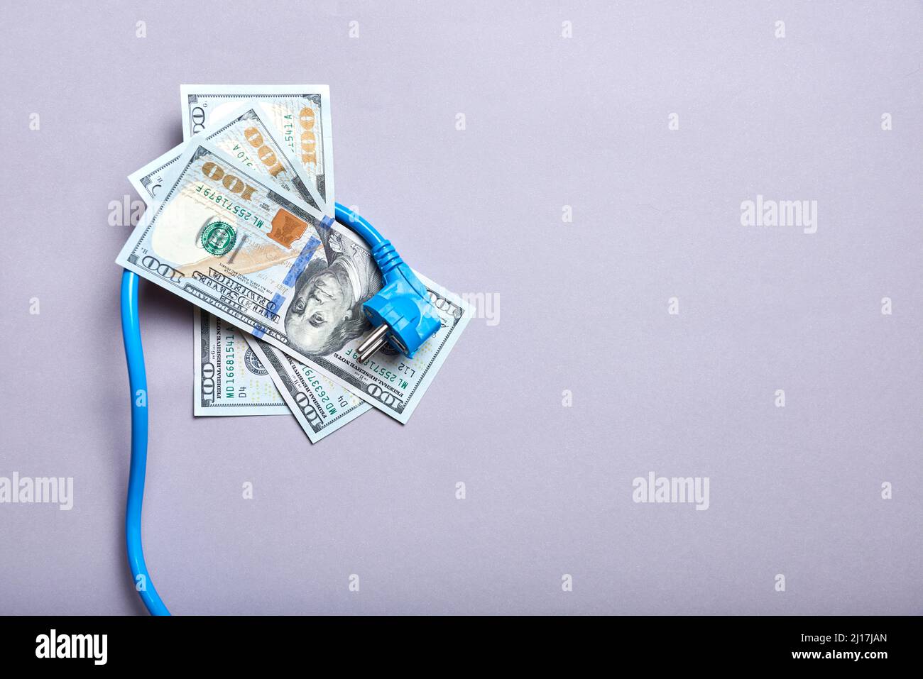 Konzeptionelles Bild über die hohen wirtschaftlichen Kosten von Strom und die Zunahme der Energiepreise: Ein Stromkabel und Dollar-Banknoten. Stockfoto