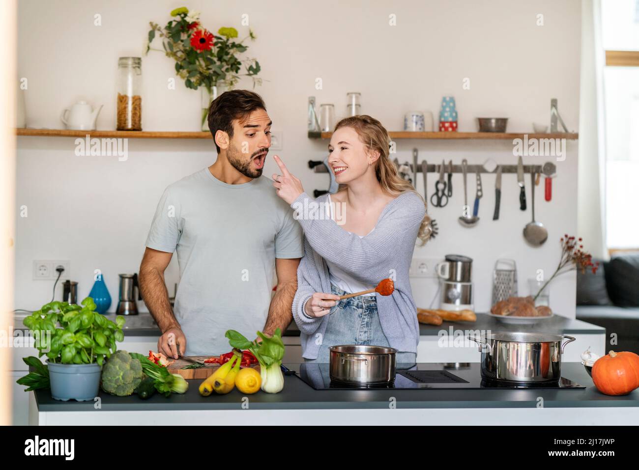 Lächelnde junge Frau, die ihrem Freund zu Hause in der Küche Nahrung zuführt Stockfoto