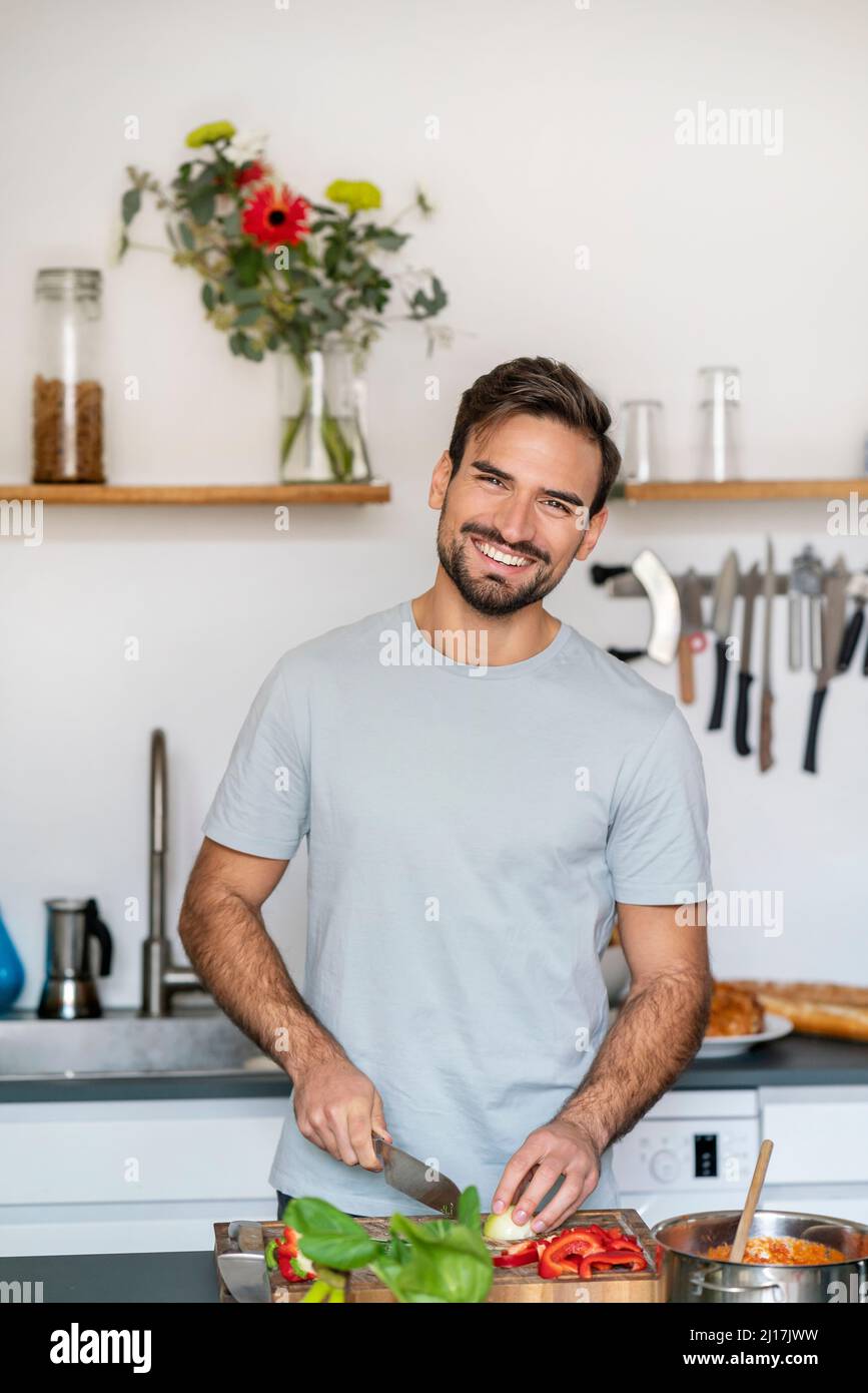 Glücklicher junger Mann, der zu Hause in der Küche Essen hackt Stockfoto