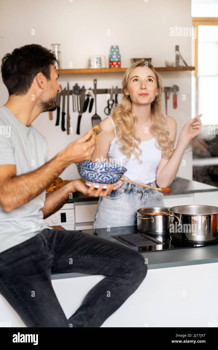 Junger Mann, der seine Freundin beim Essen in der Küche ansieht Stockfoto