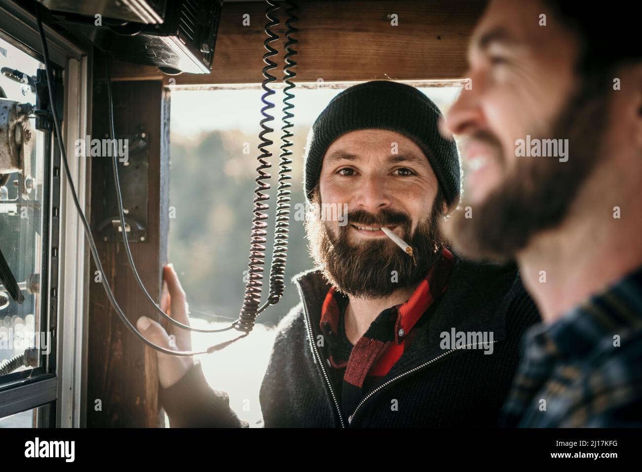 Mann, der Zigarette raucht, steht mit einem Freund im Kontrollraum des Bootes Stockfoto