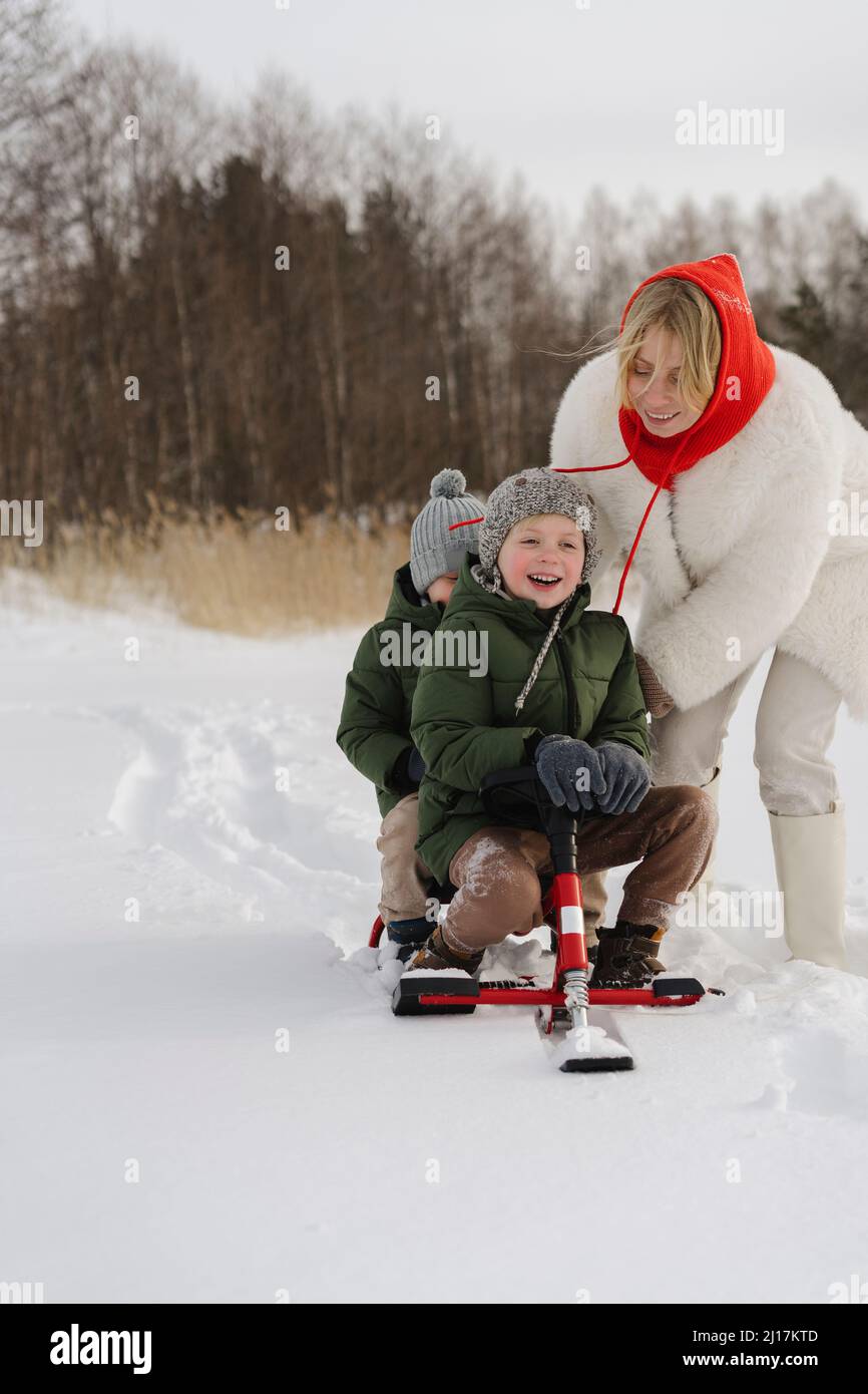 Glückliche Mutter schiebt im Winter Söhne auf dem Rodel Stockfoto