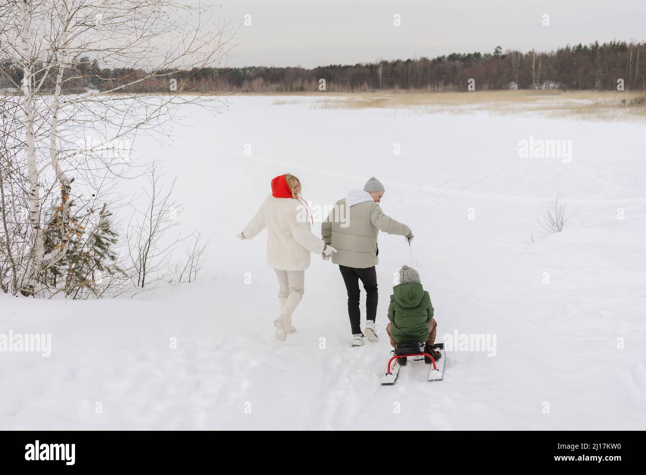 Junge auf Rodel sitzend, gezogen vom Vater, der mit Frau auf Schnee läuft Stockfoto