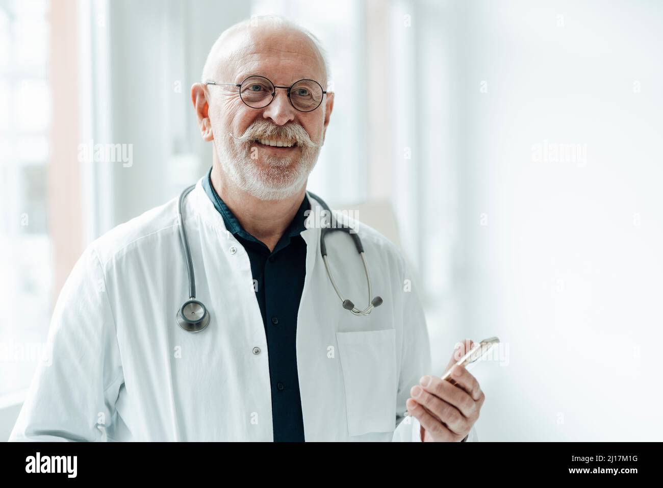 Lächelnder Oberarzt mit Smartphone im Krankenhaus Stockfoto